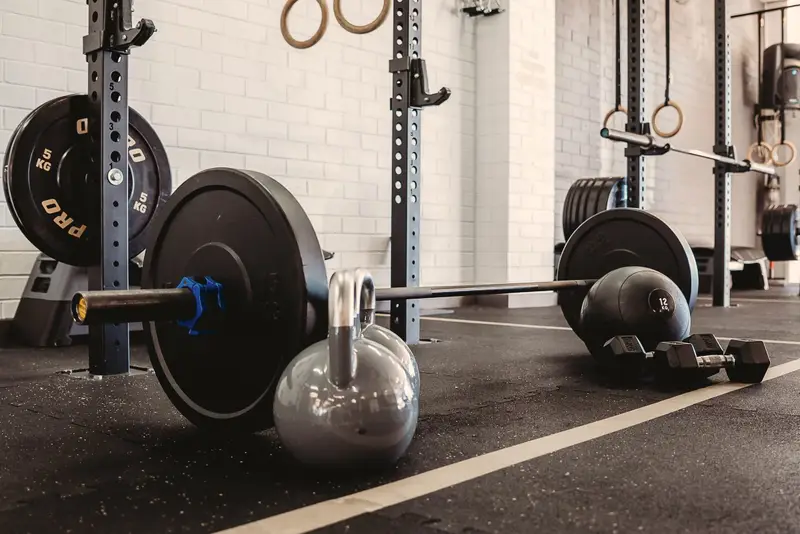 Close-up at floor level of a loaded barbell, a kettlebell, a slam ball and dumbbells on the gym floor.