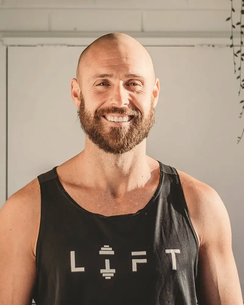 Coach Chris Goodall smiles at the camera in a black LIFT singlet.