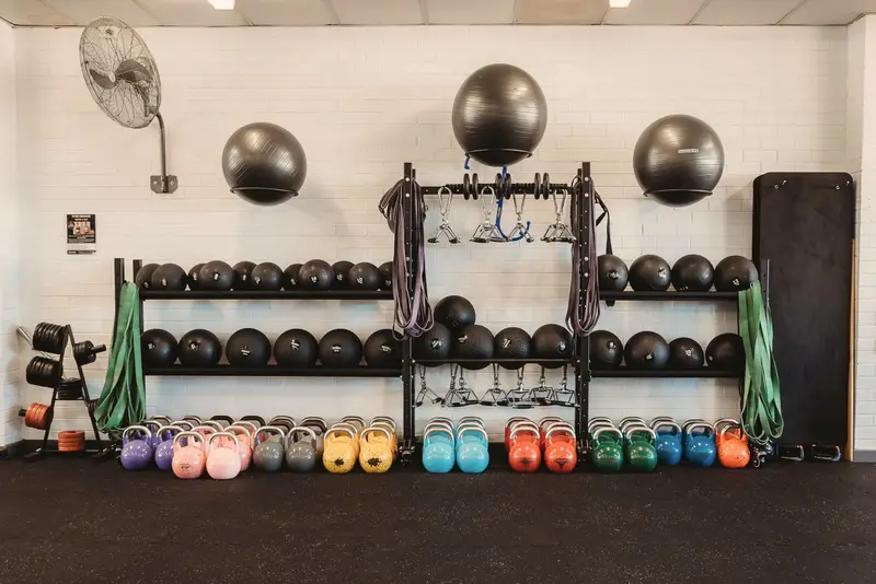 A storage wall with slam balls, resistance bands, exercise balls and a row of colourful kettlebells.