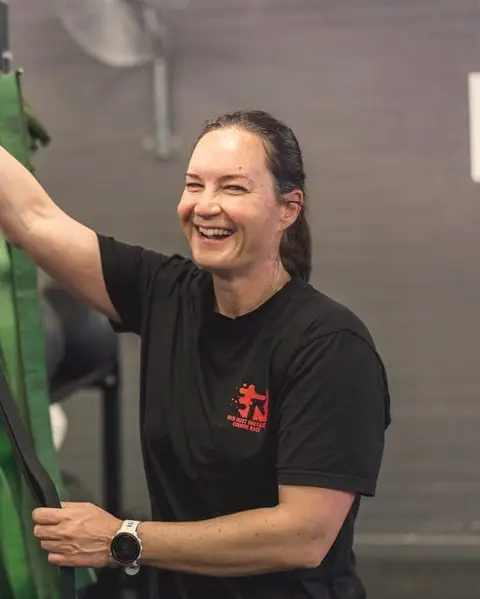 A laughing woman picks a resistance band from a rack of coloured bands.