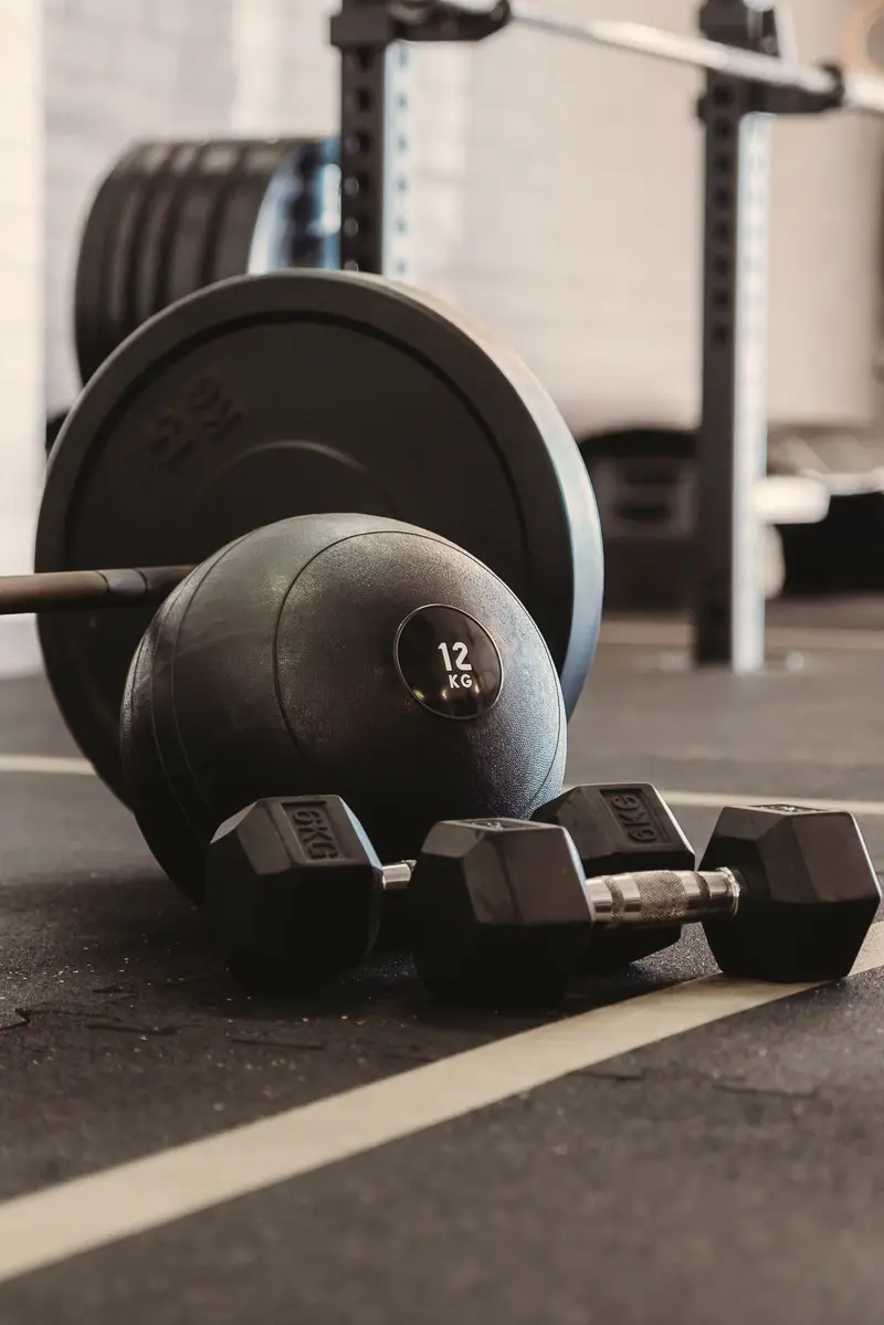 Close-up of a weight plate, a 12 kg slam ball and a pair of dumbbells on the gym floor.